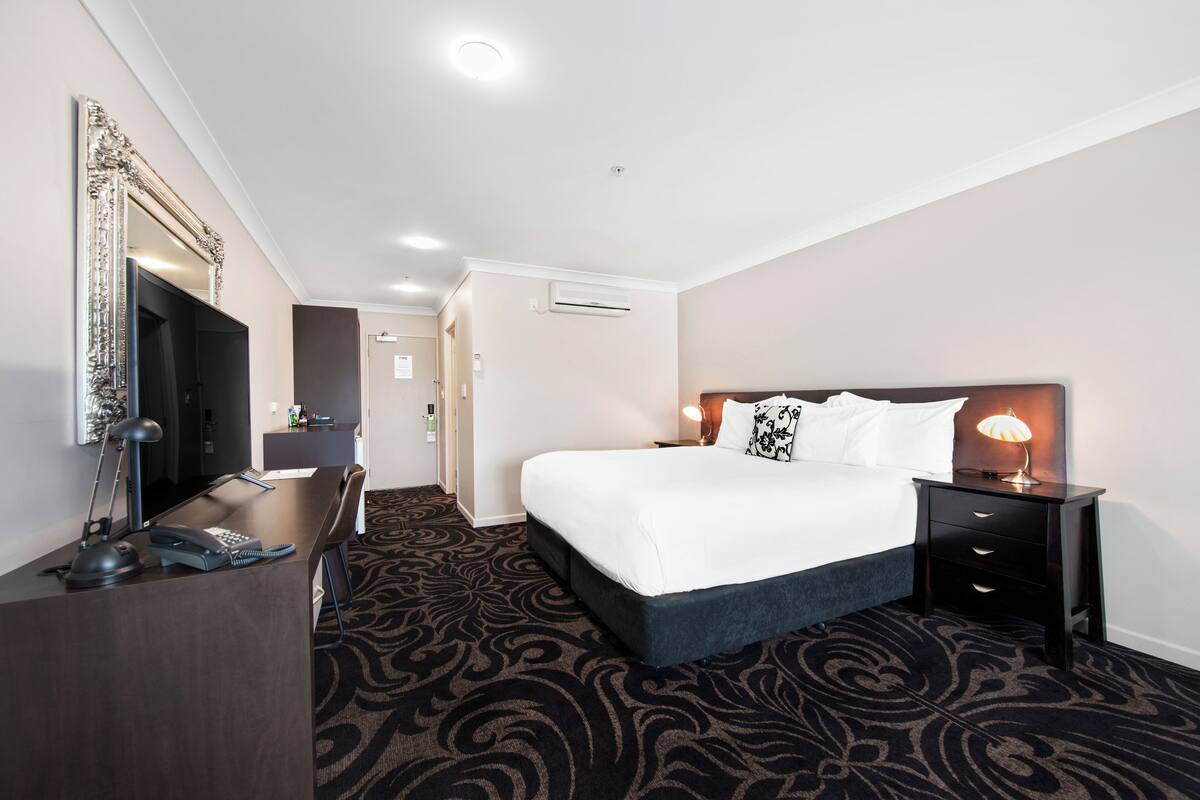 Habitación de hotel con una cama grande, un escritorio con teléfono y lámpara, un espejo y piso alfombrado.