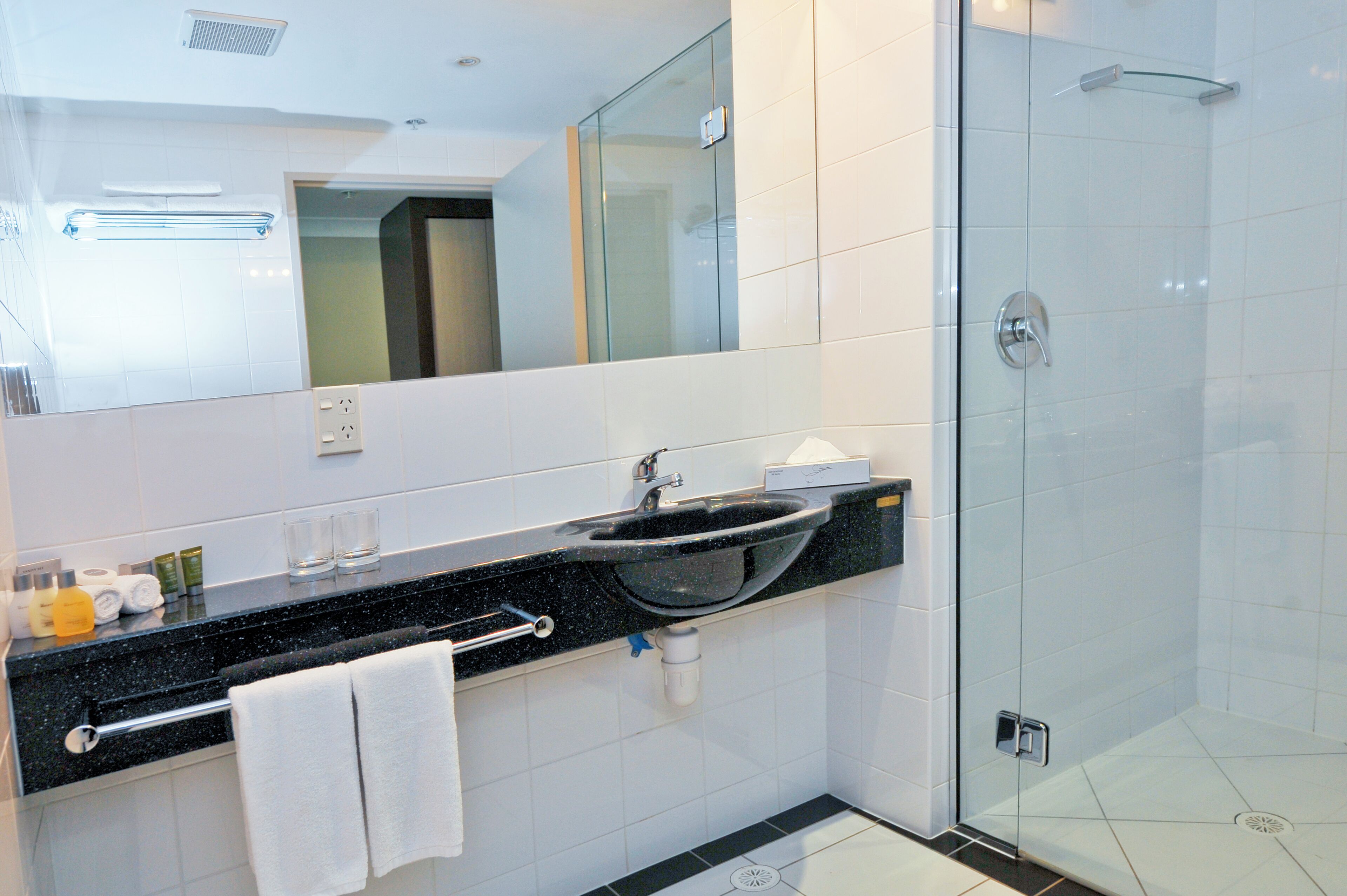 A modern bathroom with a black sink, white tiles, a glass shower enclosure, and a large mirror.