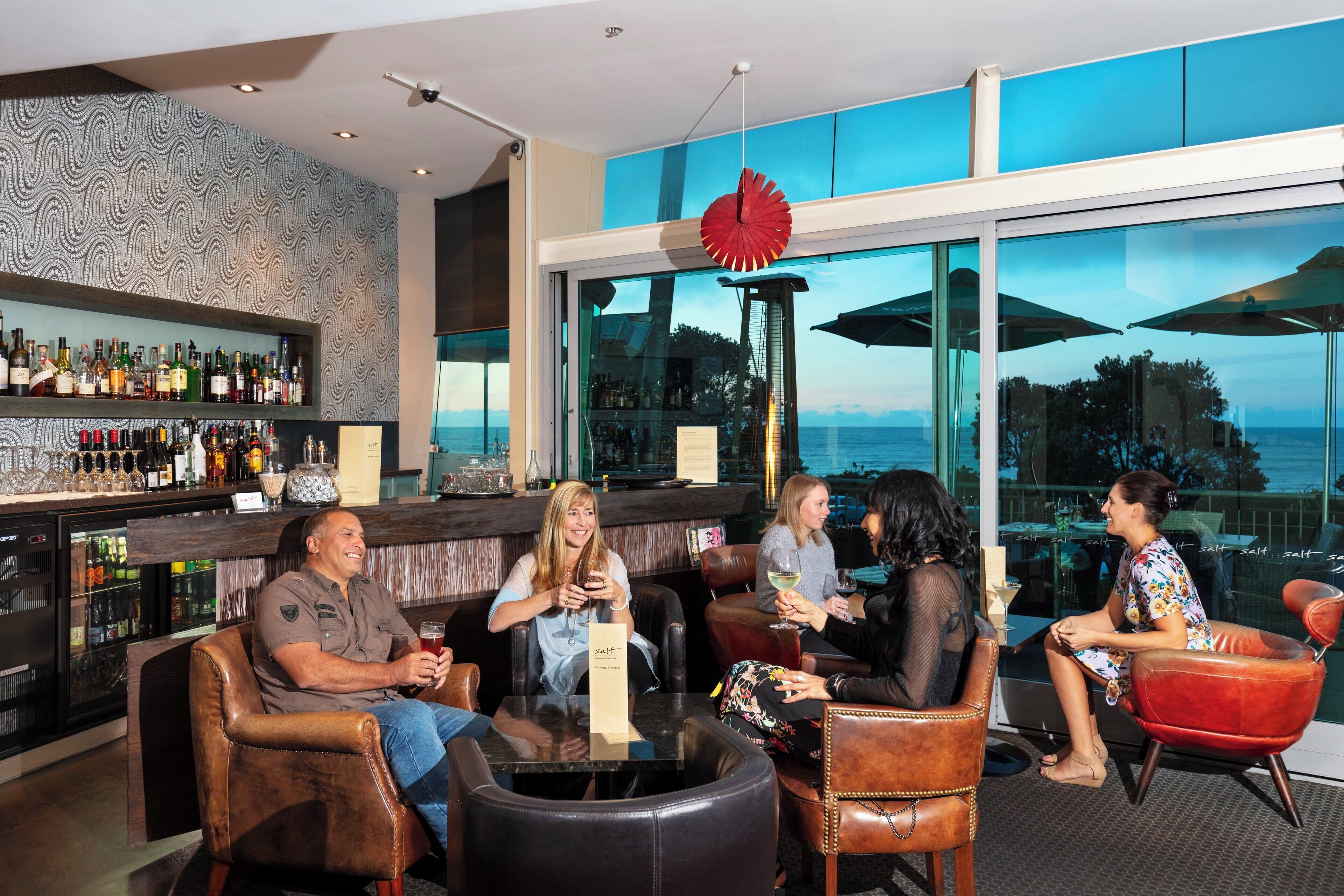 A bar area with leather chairs, a glass-top table, and a view of the ocean.