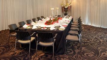 Un salón de conferencias con una larga mesa dispuesta para una reunión. Hay sillas alrededor de la mesa y un jarrón con flores sobre ella.