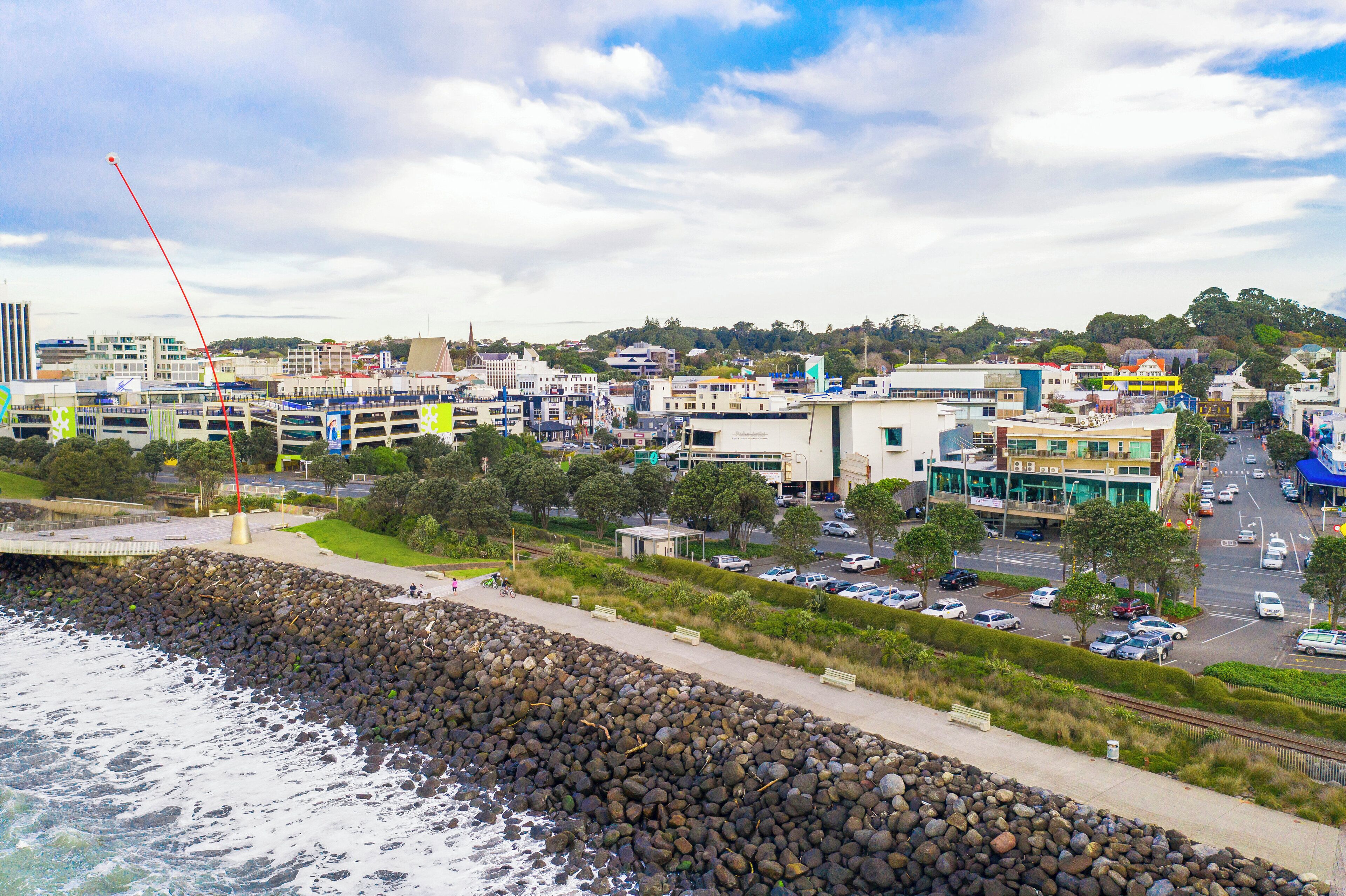 A coastal cityscape with a rocky shoreline, modern buildings, and a busy street.