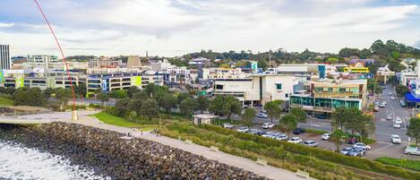 A coastal cityscape with a rocky shoreline, modern buildings, and a busy street.