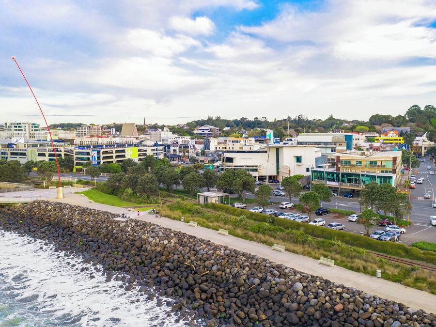 A coastal cityscape with a rocky shoreline, modern buildings, and a busy street.