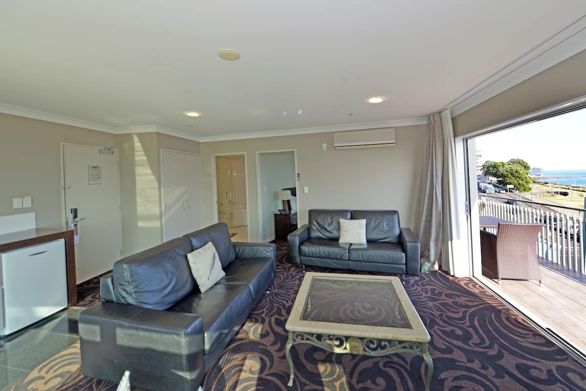 Una habitación de hotel con sala de estar, dos sofás, una mesa de centro y un balcón con vistas.