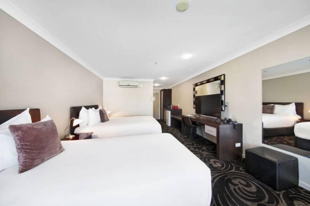 Habitación de hotel con dos camas, un escritorio, una silla, un espejo y piso alfombrado.