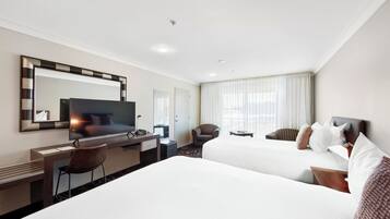 Une chambre d’hôtel avec deux lits, un bureau, une chaise, une télévision et un grand miroir.