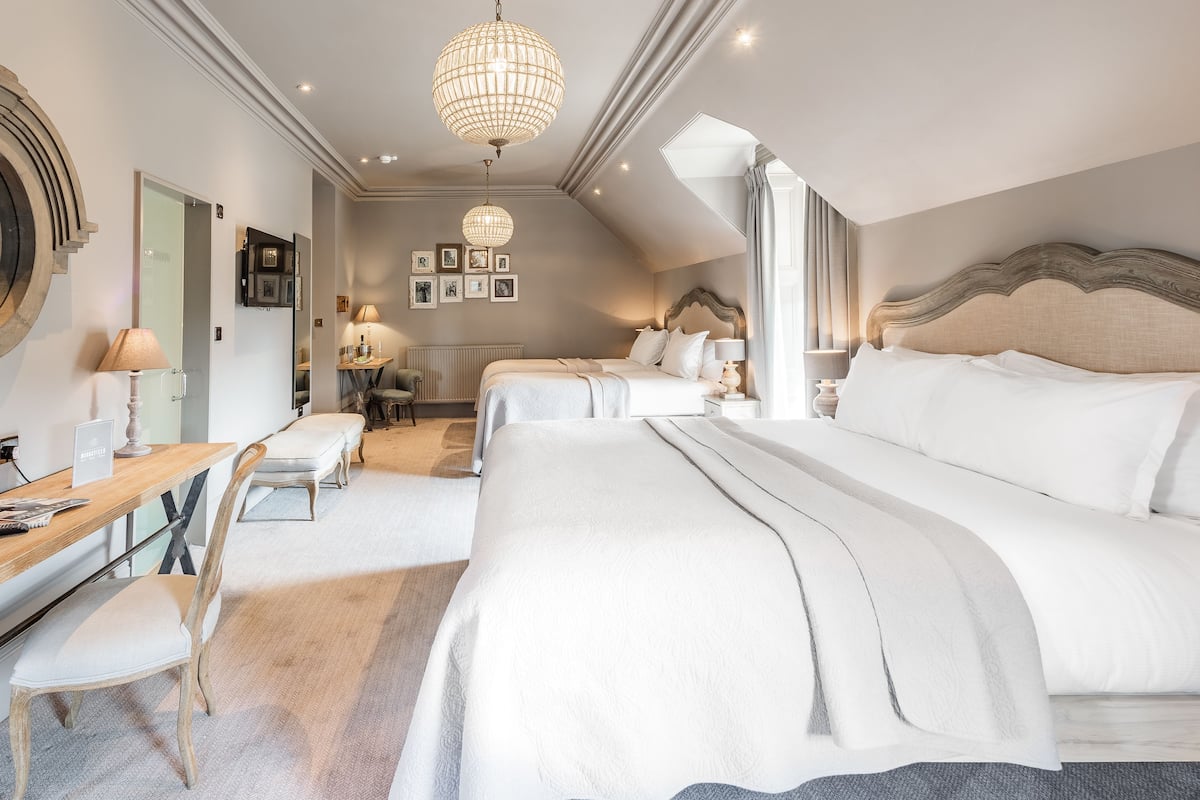 Ein geräumiges Schlafzimmer mit einem großen Bett, einem Schreibtisch und einem Sessel. Es gibt mehrere Betten im Raum, und eine Chandelier hängt von der Decke.