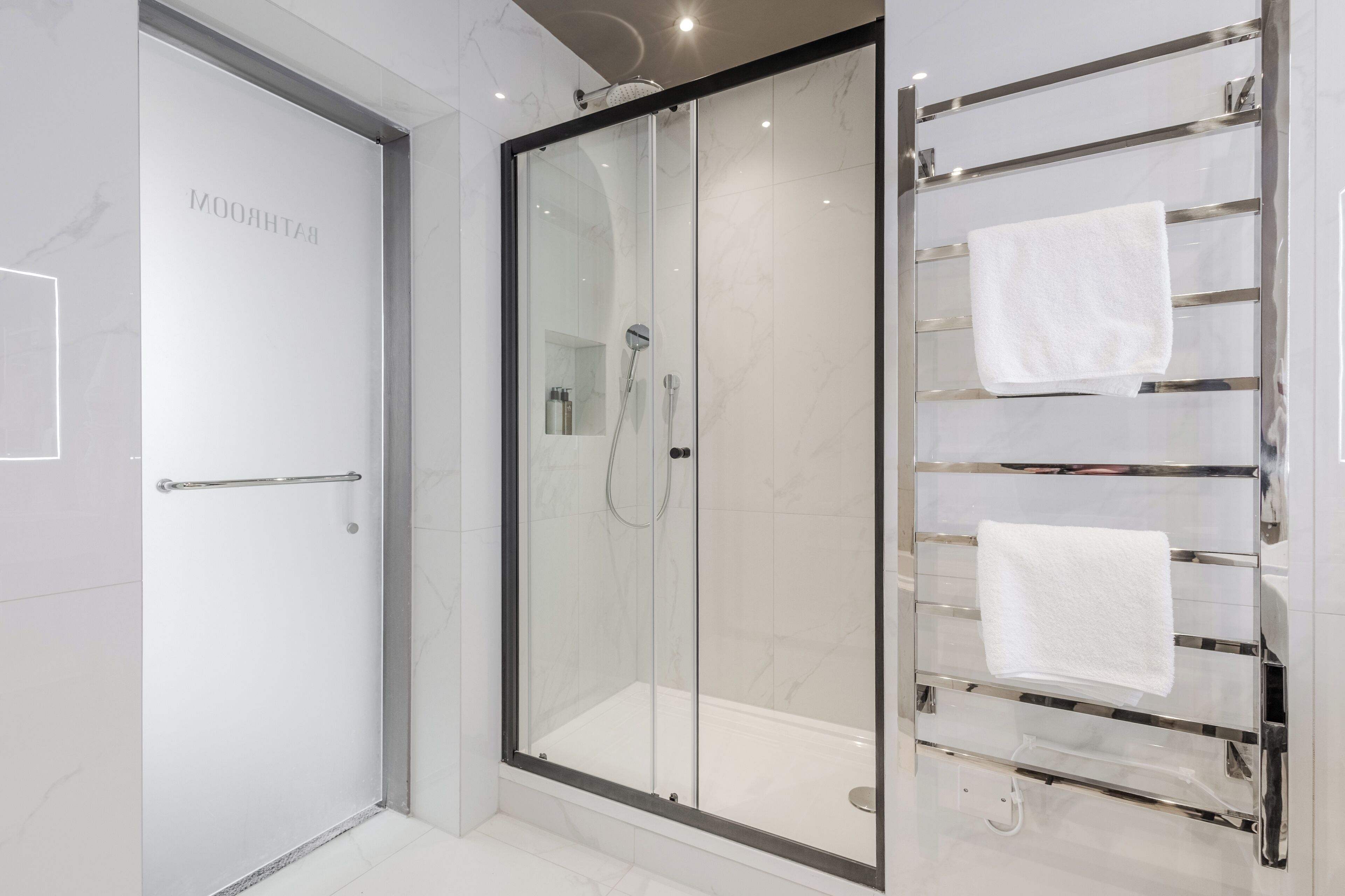 A modern bathroom with a glass-enclosed shower, a glass door, and a towel rack with two white towels.