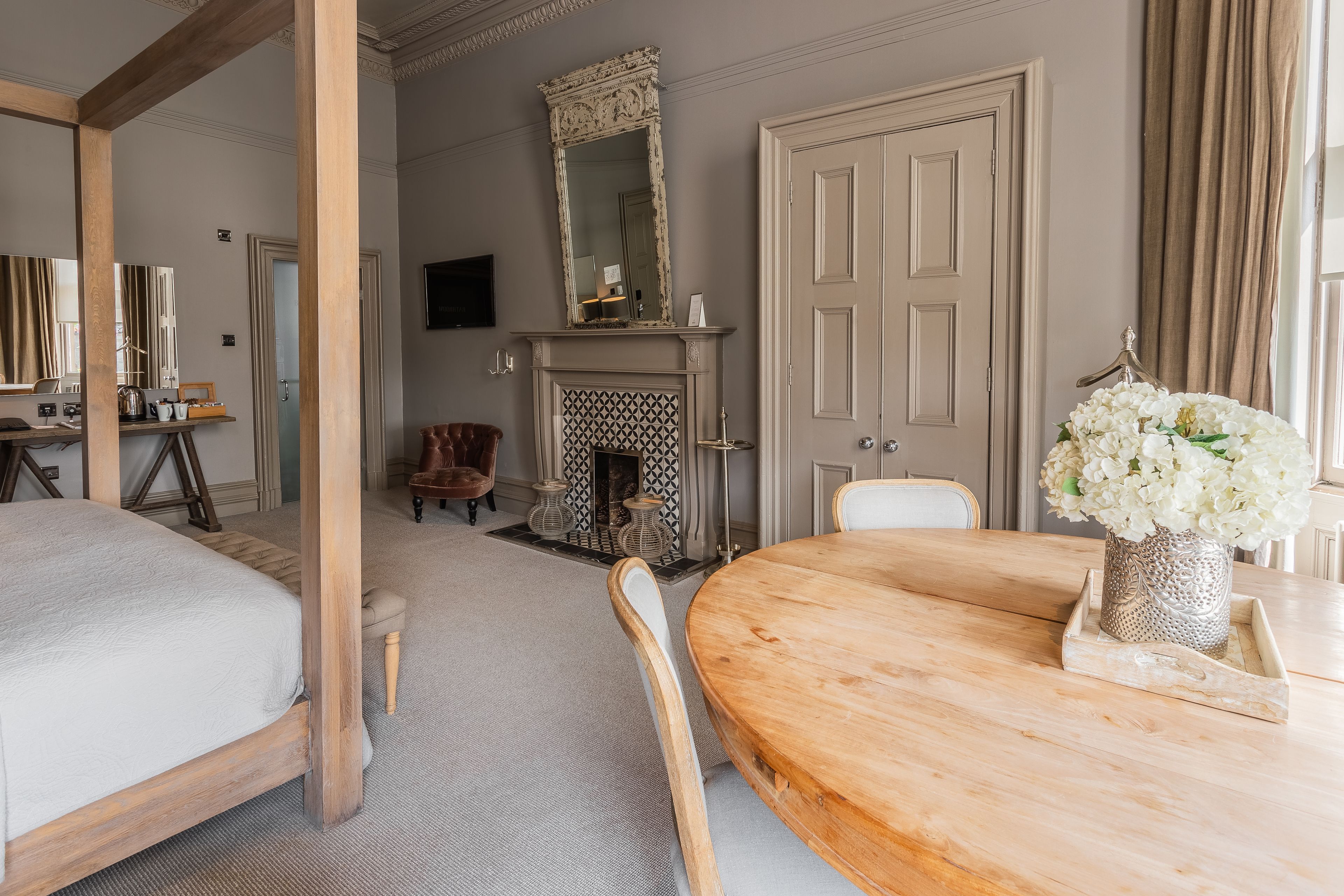 A bedroom with a large bed, a wooden table, a fireplace, and a mirror.