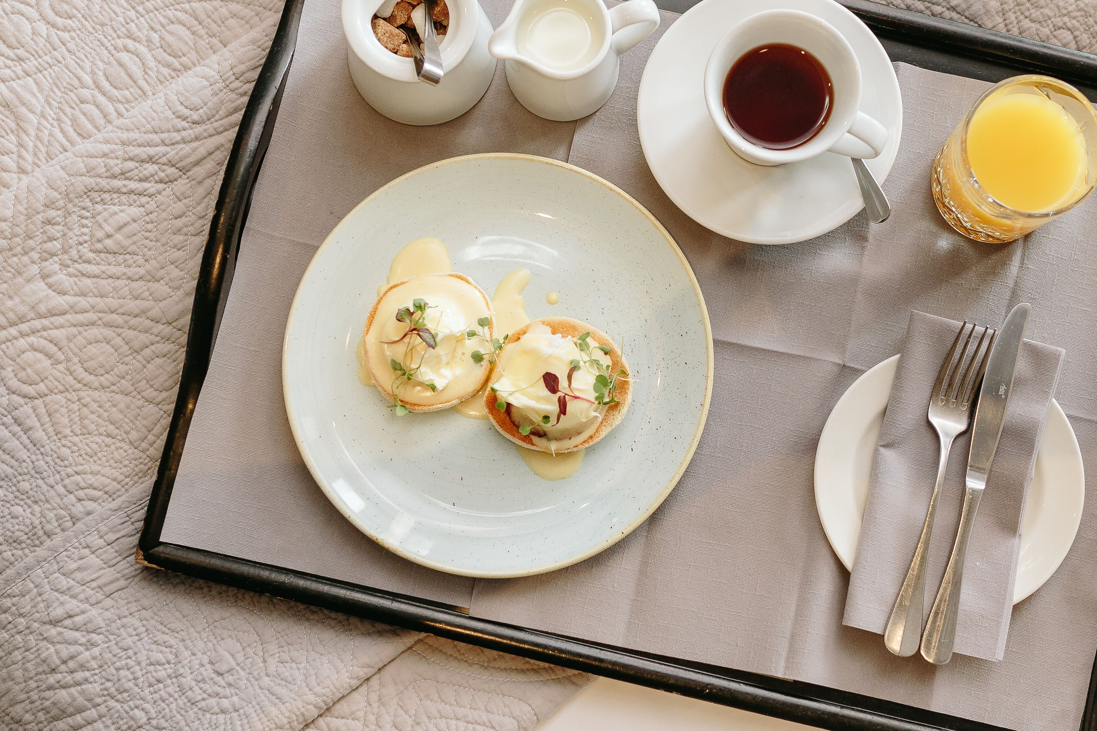 A breakfast tray with eggs benedict, coffee, and orange juice.