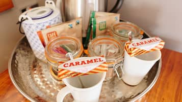 A tray with jars labeled "CARAMEL" and a white mug, a blue and white teapot, and a silver kettle on a metallic tray.