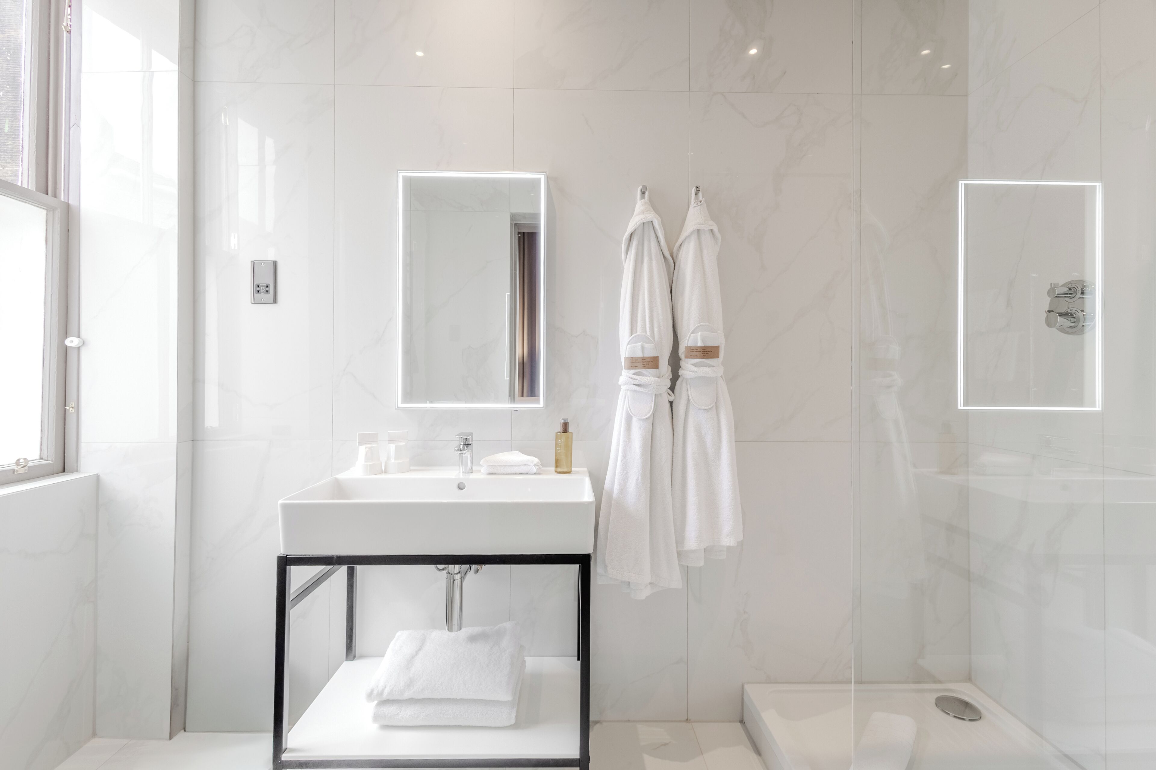 Un baño moderno con lavamanos blanco, espejo y cabina de ducha de vidrio.