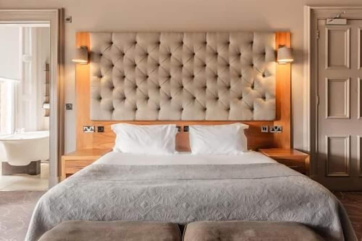 Ein Hotelzimmer mit einer gepolsterten Kopfteile, zwei Nachttischlampen, einem großen Bett mit einem gemusterten Bettüberwurf und einem Nachttisch aus Holz.