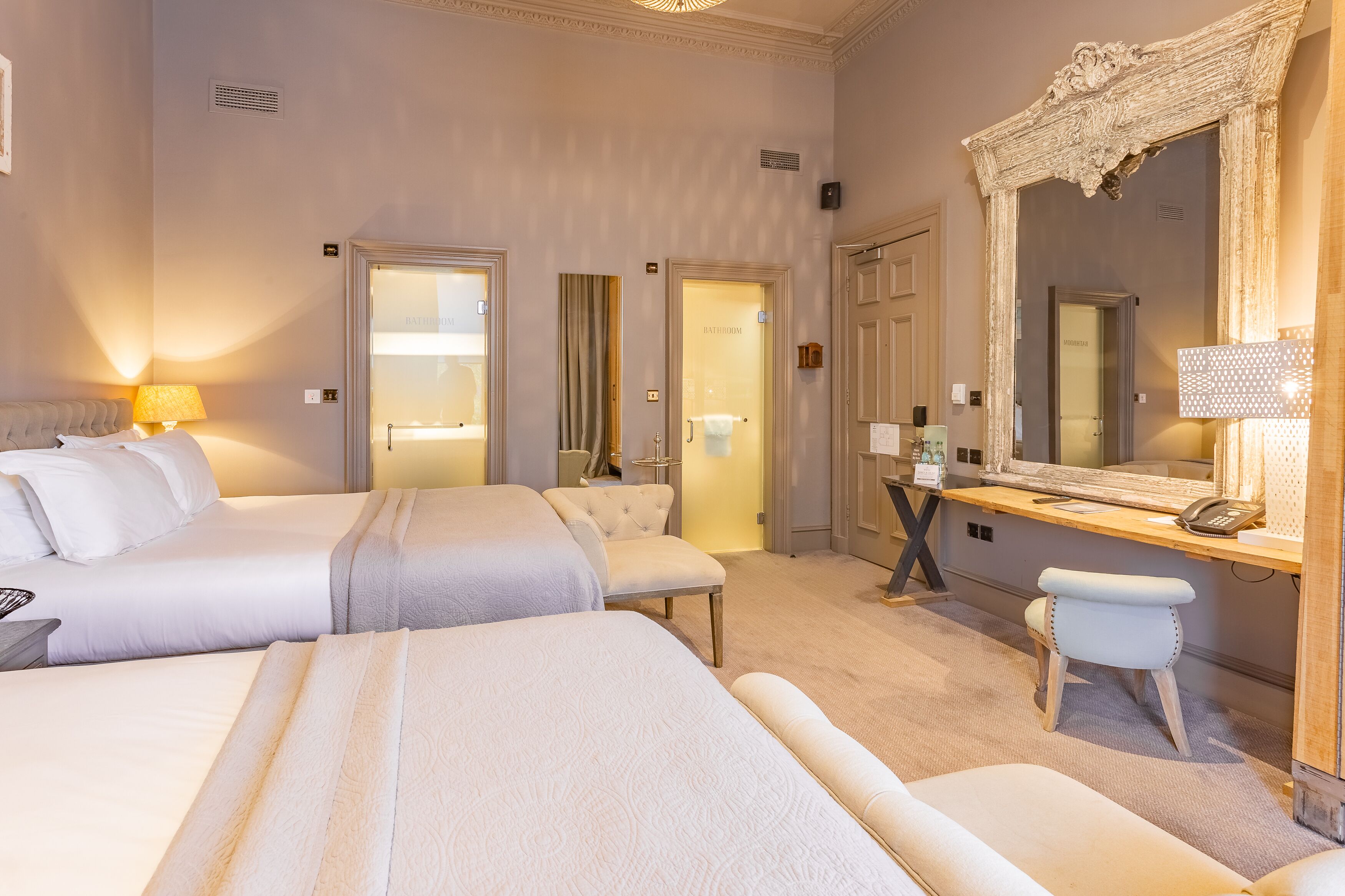 A hotel room with two beds, a desk with a telephone, and a large mirror.