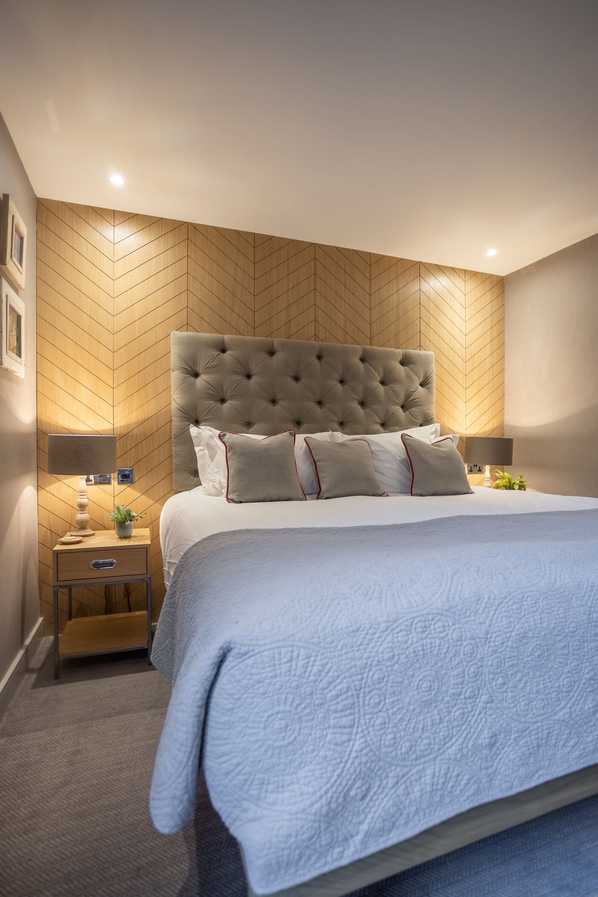 A neatly arranged bedroom with a large bed, two bedside tables, and a wooden herringbone-patterned wall.