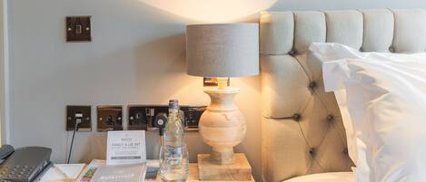 Et hotelværelse med en seng, et natbord med lampe, telefon, notesbog og en brochure.
