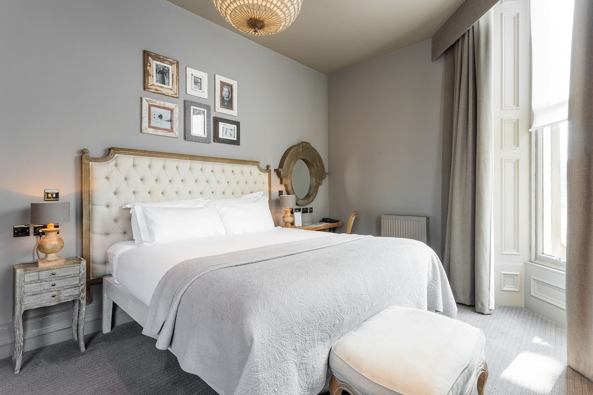 Ein ordentlich eingerichtetes Schlafzimmer mit einem großen Bett, Nachttischen, einem Spiegel und gerahmten Bildern an der Wand.
