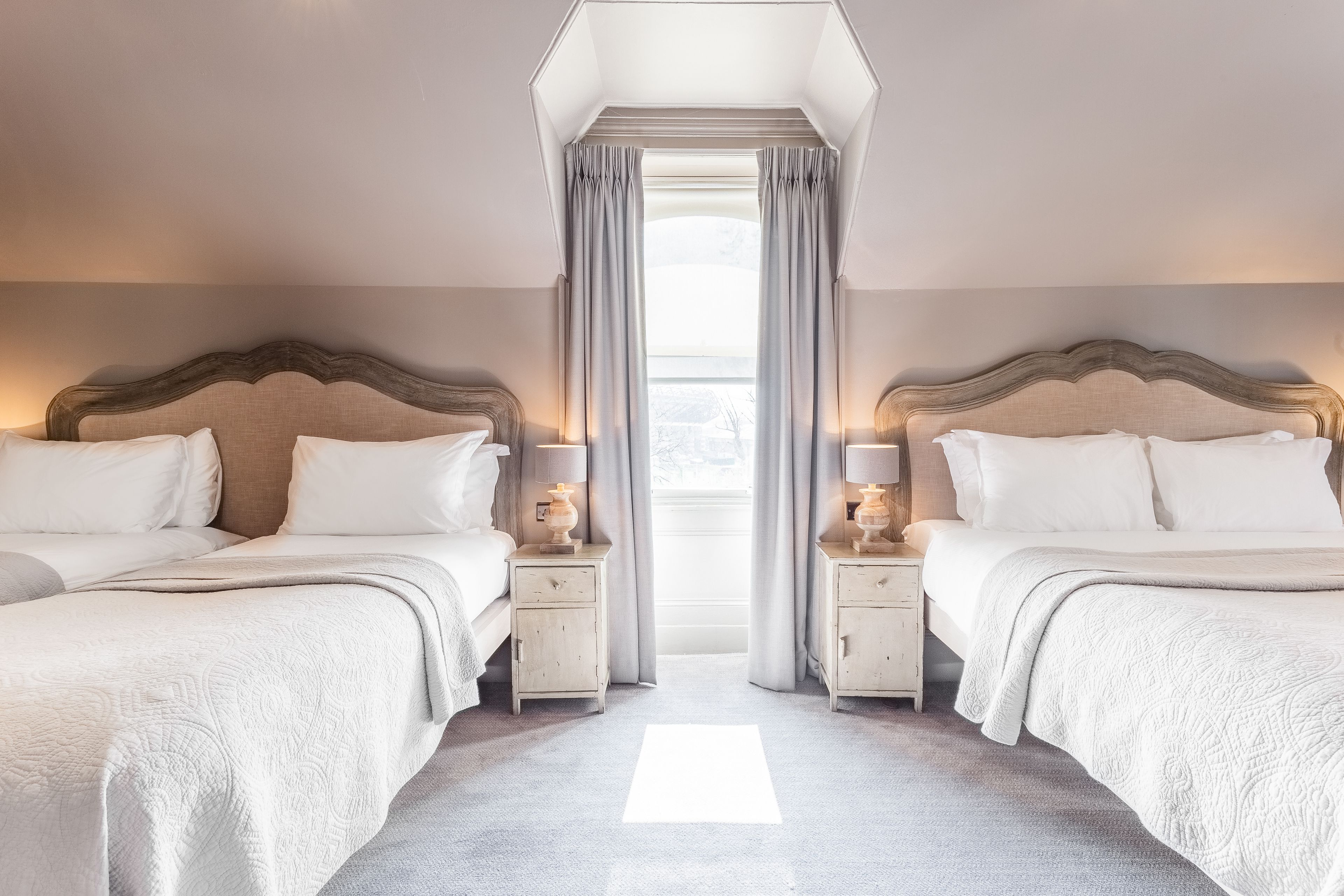 Een hotelkamer met twee bedden, een groot raam met gordijnen en een lichtgekleurd tapijt.