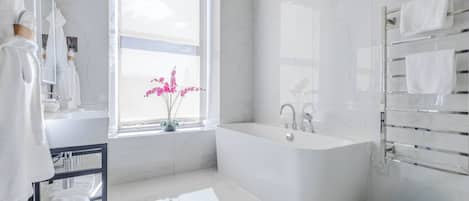 Een moderne badkamer met een bad, een raam met bloemen en een handdoekhouder.
