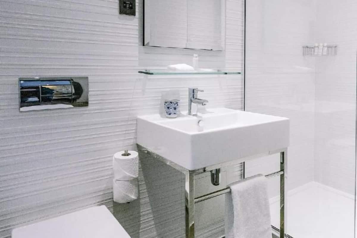 Ein modernes Badezimmer mit Toilette, Duschkabine aus Glas, Waschbecken mit Spiegel und einem Handtuchhalter.