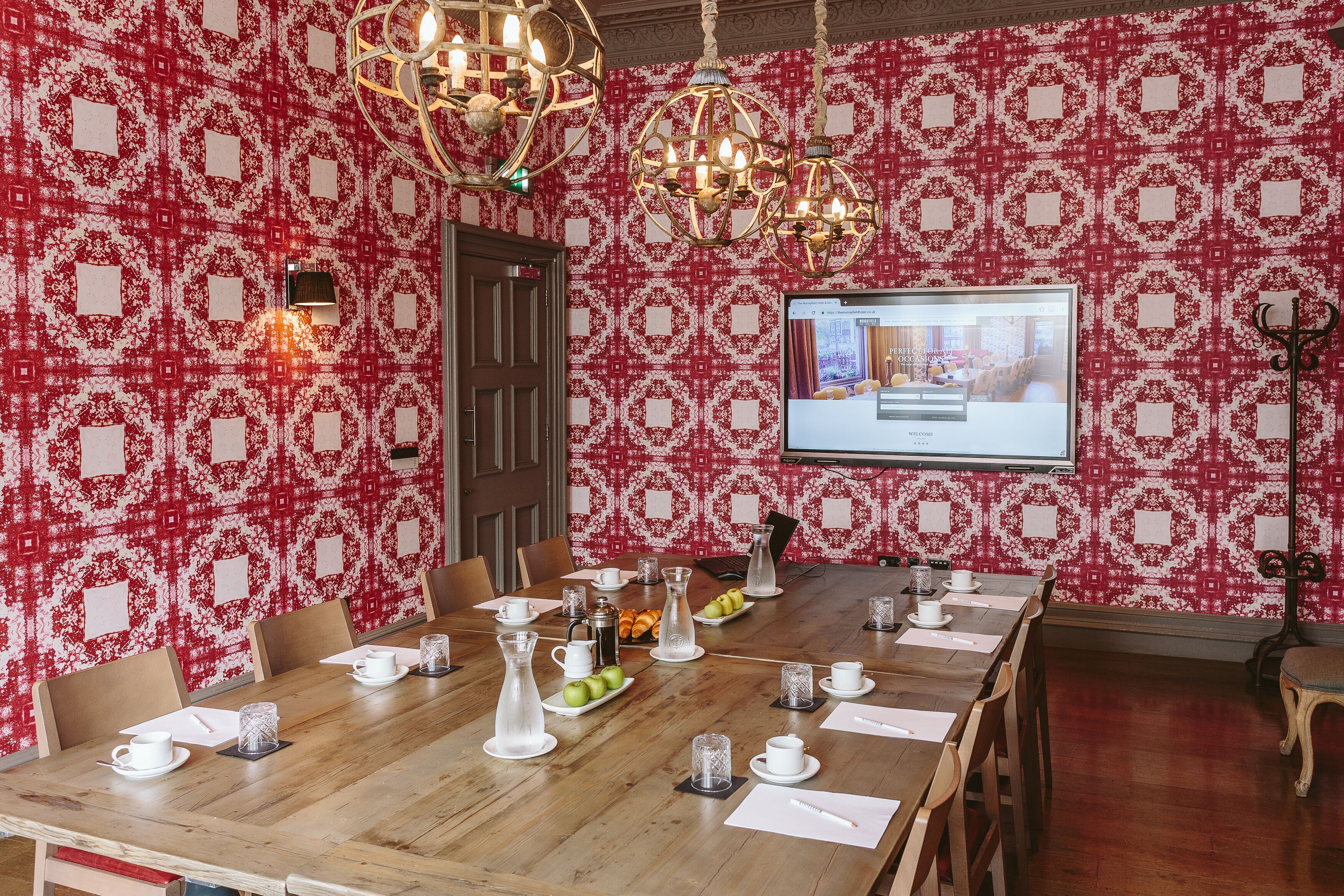 Une salle de conférence avec une table en bois préparée pour une réunion, un grand écran diffusant une présentation et un papier peint à motifs.