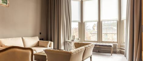 A room with a large bay window, a sofa set, a coffee table, and a radiator.