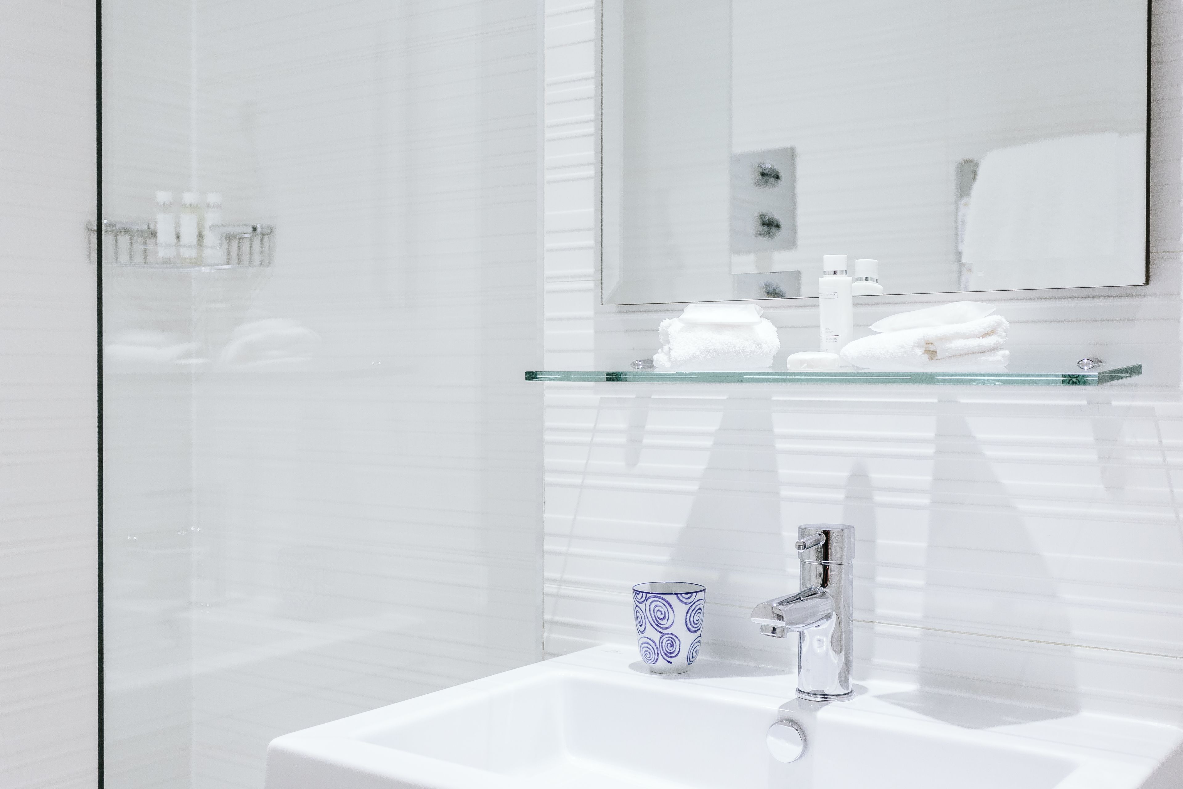 Een moderne badkamer met een glazen plankje met toiletartikelen, een witte wastafel en een spiegel erboven.