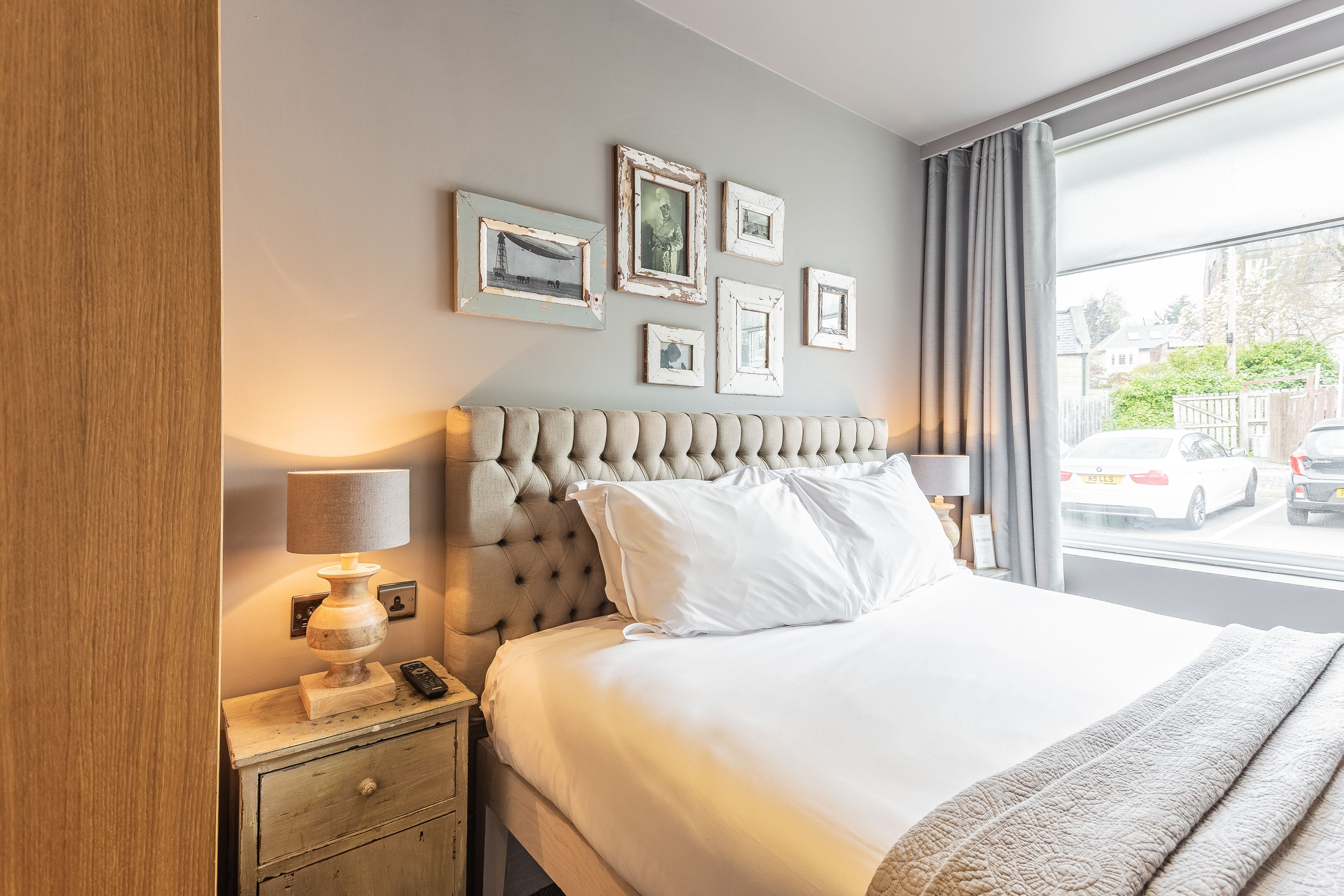 A hotel room with a large bed, a nightstand with a lamp, and a window with a view of the street.