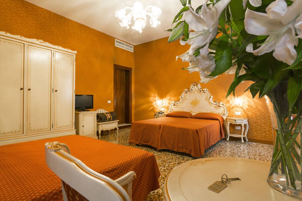 Una habitación de hotel con dos camas, un televisor, una mesita y un florero con flores.