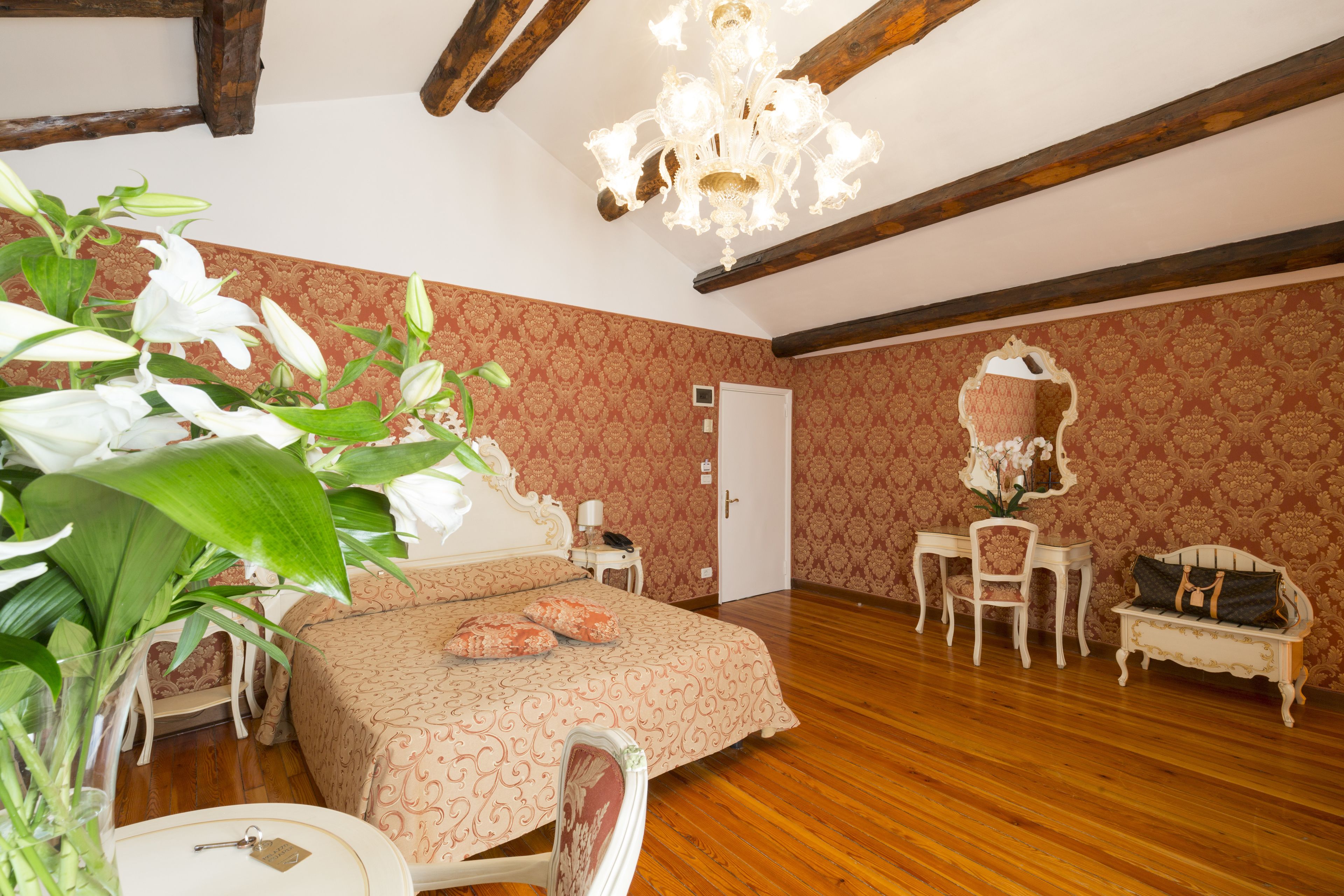A bedroom with a wooden floor, a bed with a patterned bedspread, a desk with a chair, a mirror, and a hanging light fixture.