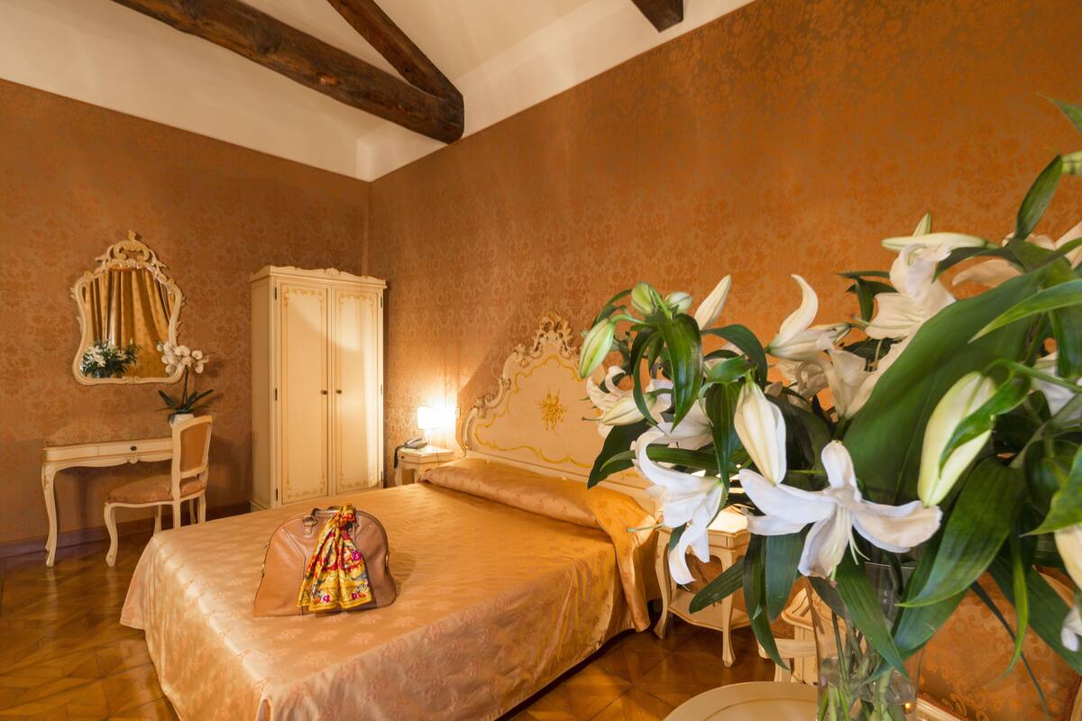 Un dormitorio con cama, escritorio, silla, armario y un jarrón con flores.