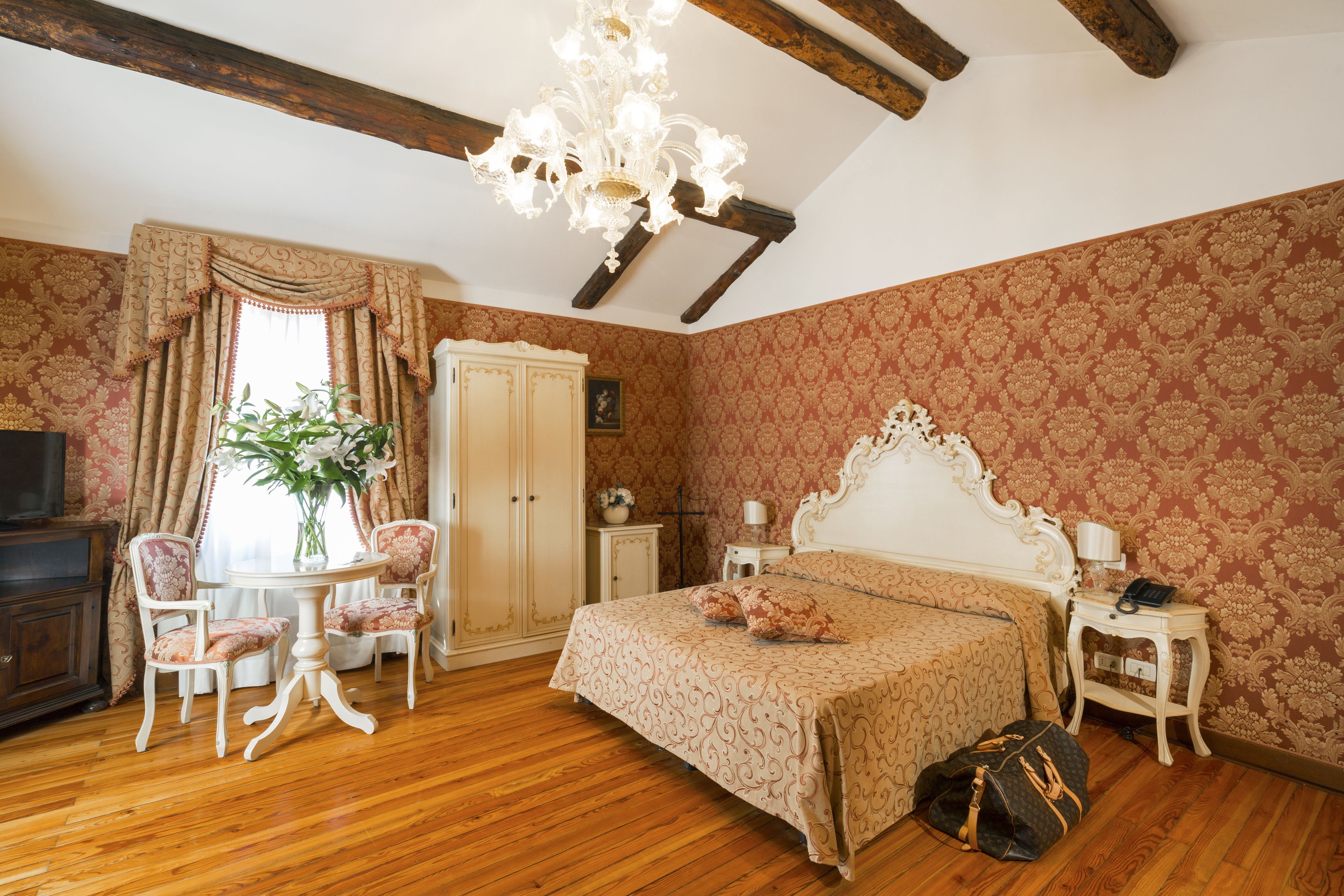 Un dormitorio con cama, mesita de noche, cómoda, silla, mesa y una araña.