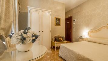 Une chambre d’hôtel avec un lit, une table de chevet avec une lampe, une petite table avec un vase de fleurs, une armoire et une porte.