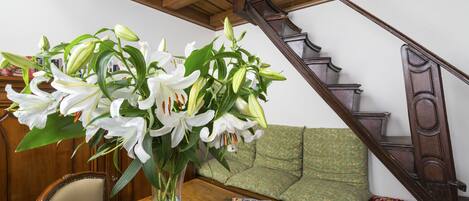A wooden table with a vase of white lilies, a green patterned sofa, and a wooden staircase.