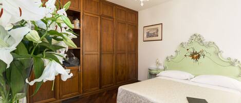 A bedroom with a wooden wardrobe, a bed with a green headboard, and a vase of white flowers.