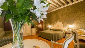 A room with a bed, a chair, a table with a vase of flowers, and a television on a cabinet. - Palazzo Guardi (Venice)