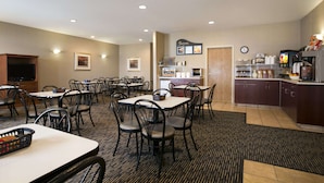 A hotel dining area with multiple tables and chairs, a kitchen area with appliances, and a clock on the wall. - Days Inn by Wyndham Moose Jaw (Moose Jaw)