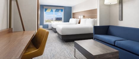 Habitación de hotel con cama, sofá azul, escritorio de madera, silla amarilla y vistas a la ciudad.
