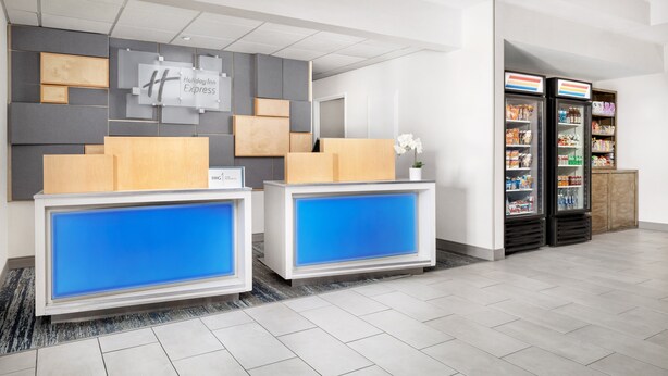 A hotel reception area with two reception desks, a wall-mounted sign, and a refrigerator stocked with snacks. - Holiday Inn Express Las Vegas - Stadium Area by IHG (Las Vegas)