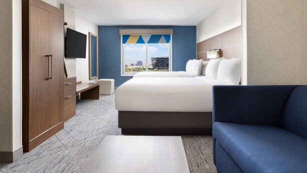 A hotel room with a bed, a blue sofa, a TV, and a wardrobe. - Holiday Inn Express Las Vegas - Stadium Area by IHG (Las Vegas)
