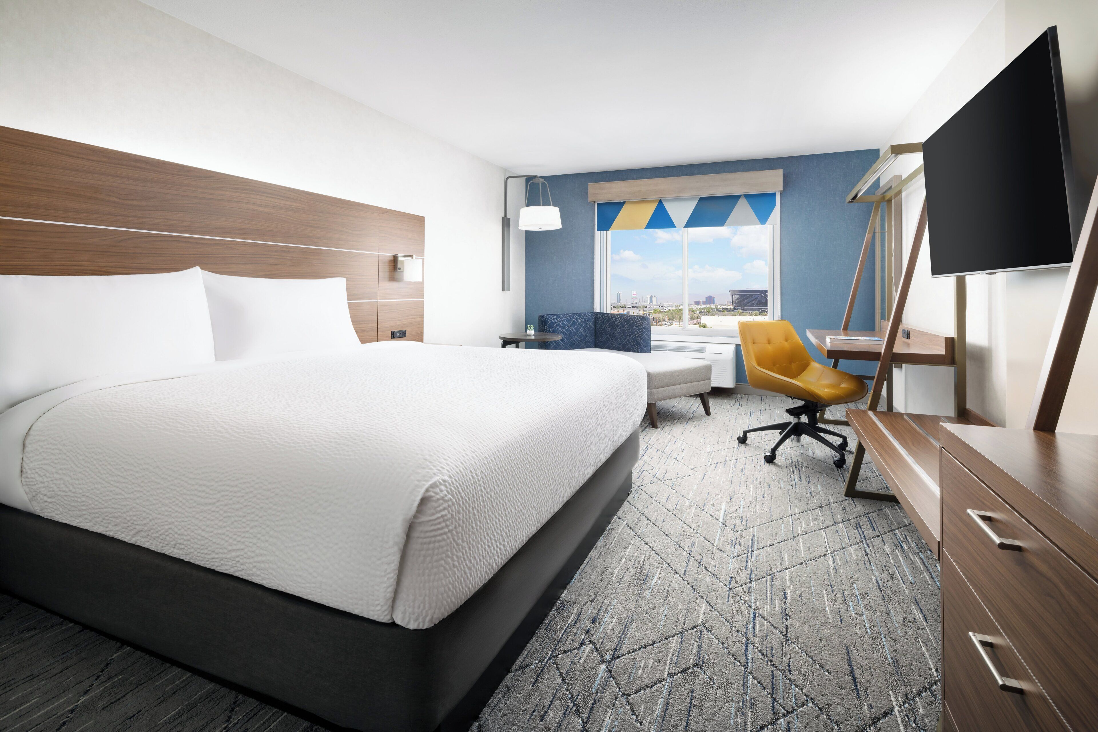 Een hotelkamer met een groot bed, een bureau, een stoel, een televisie en een raam met uitzicht op de stad.
