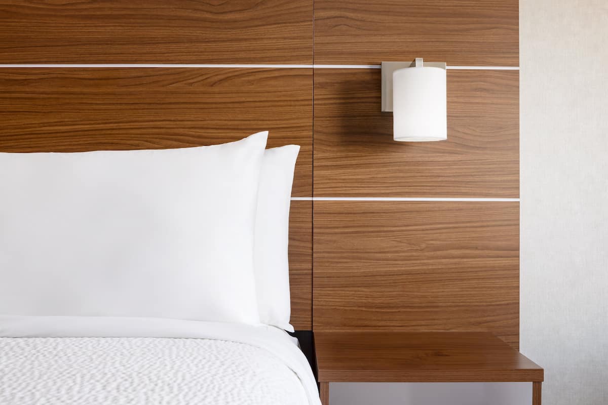 A neatly made bed with white linens, a wooden headboard, and a bedside table with a white lamp.