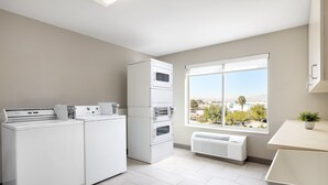 A laundry room with stacked washers and dryers, a window with a view of a cityscape, and a small plant on a counter. - Holiday Inn Express Las Vegas - Stadium Area by IHG (Las Vegas)
