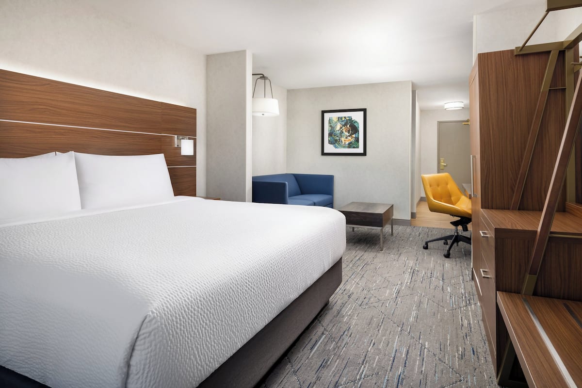 A hotel room with a large bed, a desk, a chair, and a wardrobe.