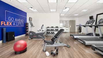 A modern gym with treadmills, a bench press, dumbbells, and a red exercise ball.