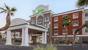 Edificio de Holiday Inn Express con entrada cubierta, palmeras y estacionamiento.