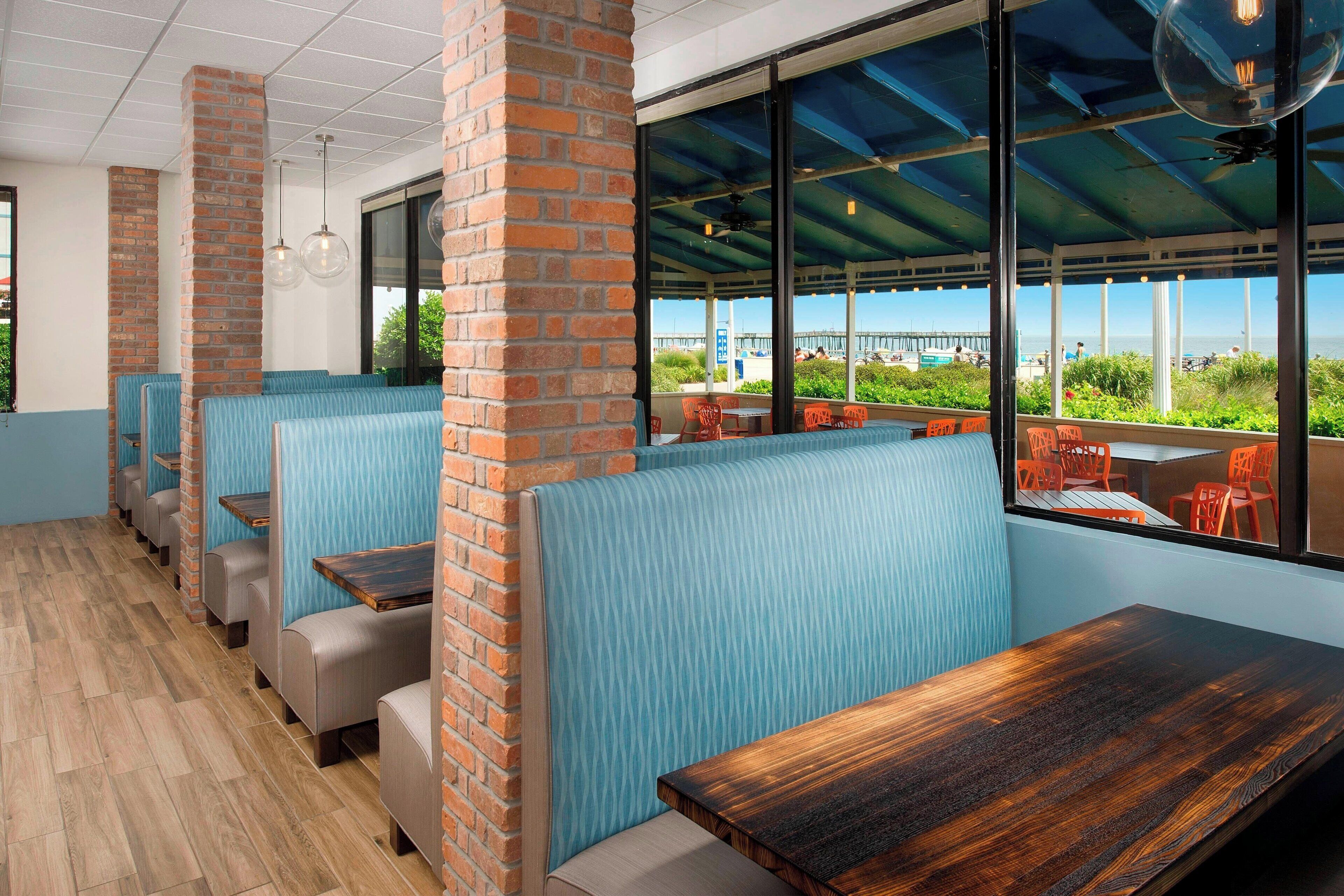 Ein Restaurant mit Ziegelpfeilern, blau gepolsterten Sitzecken und großen Fenstern mit Blick auf die Stadt.