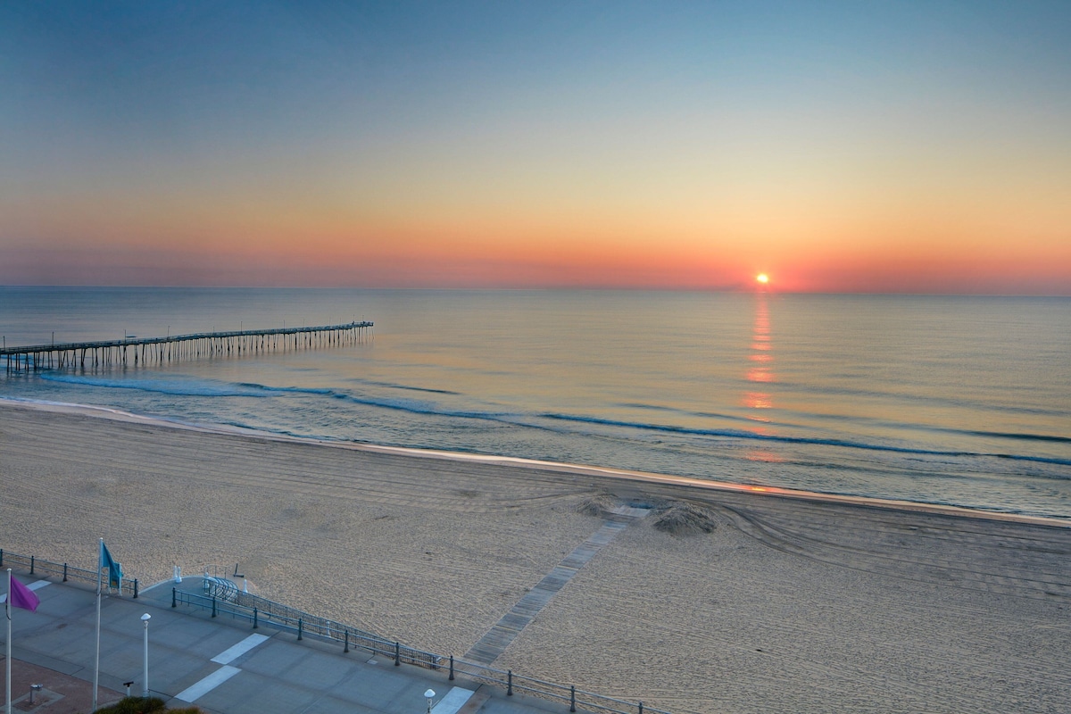 A beach with a pier extending into calm waters during sunset.