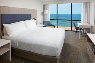 Quarto de hotel com uma cama grande, uma escrivaninha, uma cadeira e vista para o oceano.