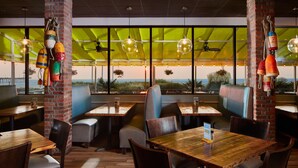 A restaurant with wooden tables and chairs, brick pillars, and large windows offering a view of the ocean. - Four Points By Sheraton Virginia Beach Oceanfront (Virginia Beach)